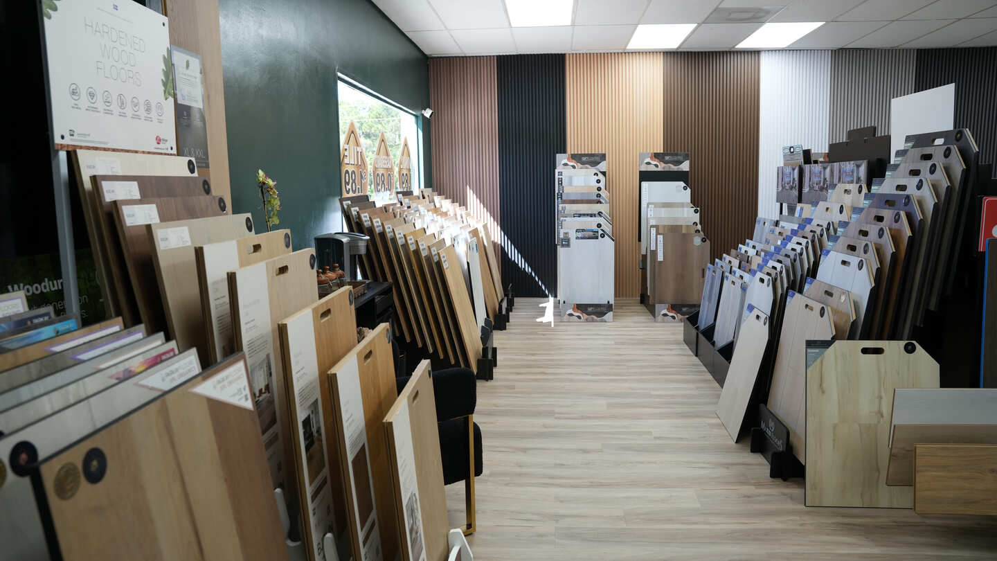 Aisle view in the PSL Floor & Supply showroom, lined with hardwood and vinyl plank flooring samples.