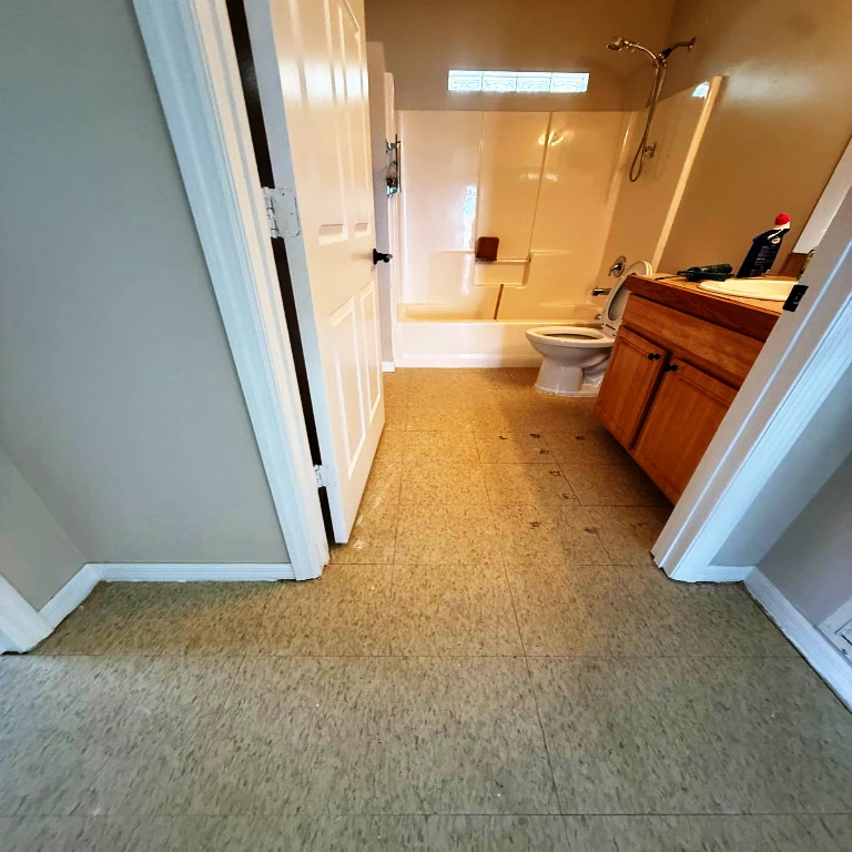 Original Bathroom State Before Rustic Pine Installation Text: Bathroom interior before renovation showing dated beige tile flooring and wooden vanity